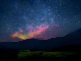 Vintergatan och rosa ljus vid bergen. natt färgglada landskap. stjärnhimmel med kullar. vackert universum. rymdbakgrund med galax. resor bakgrund foto