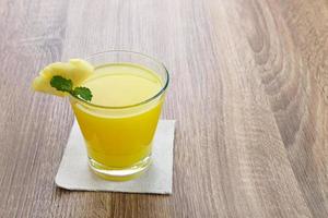 ett glas färsk ananasjuice med myntablad och skiva frukt. kallpressad juice foto