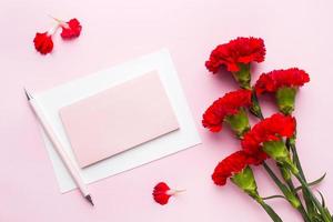 röd-rosa föremål. kopp te, nejlika blommor anteckningsblock för text på pastell rosa bakgrund. kopieringsutrymme. ovanifrån platt låg foto