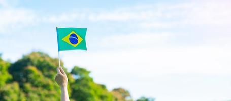 hand som håller Brasiliens flagga på blå himmel bakgrund. september självständighetsdag och glada festkoncept foto