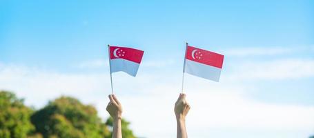hand som håller singapores flagga på blå himmel bakgrund. singapores nationaldag och glada firande koncept foto