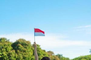 hand som håller Indonesiens flagga på blå himmel bakgrund. Indonesiens självständighetsdag, nationell helgdag och koncept för glada firande foto