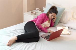 vacker kvinna som talar och arbetar med laptop på sängen