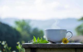 framifrån av en vit keramisk kopp varmt kaffe på ett rustikt träbord i naturlig bakgrund. morgon förfriskningar och drinkar koncept foto