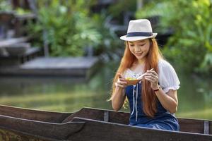ung asiatisk kvinna turist reser med träbåt på flytande marknad i Thailand och har lokal gatumat för sydostasiens turismkoncept foto