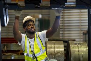 afrikansk amerikansk mekanikerarbetare kontrollerar växeln för hydraulisk maskin inuti metallståltillverkningsfabriken för underhålls- och inspektionskoncept foto
