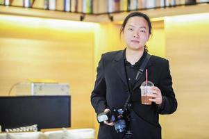 avkopplande asiatisk fotograf som håller dryck och kamera foto