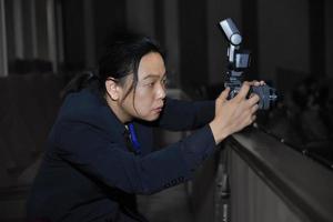 asiatisk långhårsfotograf i marin kostym koncentrerad med sin kamera. foto
