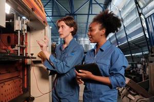 två professionella kvinnliga ingenjörsarbetare i säkerhetsuniformer arbetar genom att inspektera maskinernas spänningsström, kontrollera och underhålla elsystemserviceyrken vid tillverkningsfabriken. foto
