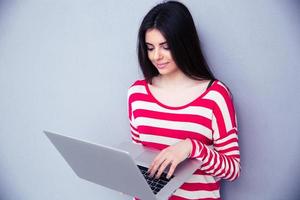 söt ung kvinna som använder bärbar dator över grå bakgrund