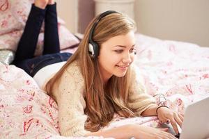 tonårsflicka liggande på sängen med bärbar dator bär hörlurar