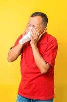 asiatisk pensionär blir sjuk, med influensa och nysningar isolerad på gul bakgrund. foto