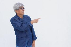 Asiatisk senior man i denim avslappnad stil pekar pekfinger isolerad på vit bakgrund med kopia utrymme. foto