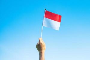 hand som håller Indonesiens flagga på blå himmel bakgrund. Indonesiens självständighetsdag, nationell helgdag och koncept för glada firande foto