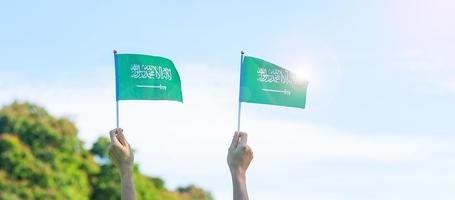 hand som håller Saudiarabien flagga på blå himmel bakgrund. september Saudiarabiens nationaldag och glada firande koncept foto