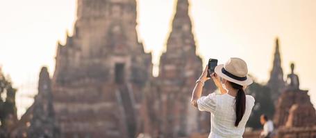 glad turistkvinna som bär kirurgisk ansiktsmask och tar foto med mobil smartphone, skyddar covid-19-pandemin under besök i ayutthaya-templet. nytt normal-, säkerhets- och resekoncept