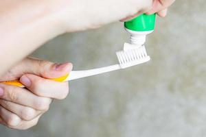 hand som håller tandborstar med tandkräm i badrummet. livsstil, daglig rutin, världens munhälsodag och gratis tanddagkoncept foto