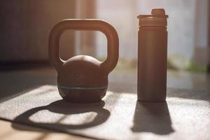 gymutrustning, kettlebell hantelvikt och flaska vatten på yogamattan hemma. foto