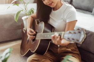 kvinna som spelar gitarr hemma. vacker kvinna ler och spelar gitarr med sina växter i vardagsrummet. foto