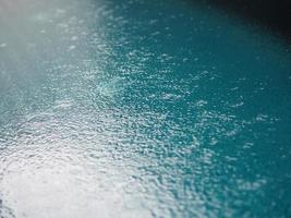regndroppar fallande blått vatten i poolbakgrunden krusar på ytstrukturen, glittrande bokeh abstrakt foto
