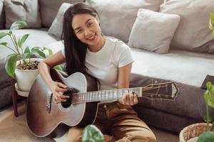 kvinna som spelar gitarr hemma. vacker kvinna ler och spelar gitarr med sina växter i vardagsrummet. foto
