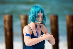 konstnärlig blåhårig kvinna performancekonstnär i klänning insmord med blå gouachefärger på hennes kropp foto