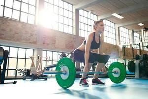 fokuserad ung kvinna som lyfter vikter i ett gym foto