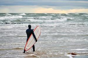 manlig surfare i baddräkt som går längs havet med surfbräda foto