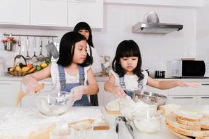 mamma söker två barn hjälp att förbereda en baka med mamma i köket foto