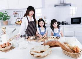 asiatisk mamma och lilla dotter bär förkläde laga mat tillsammans och le i köket foto