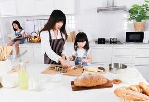 asiatisk mamma och lilla dotter bär förkläde laga mat tillsammans i köket foto