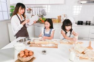asiatisk lycklig familj som lagar mat tillsammans mamma läser en bok och två pappa förbereder en baka foto