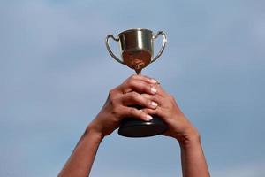 en vinnarframgång som firar med trofépris och mästarkoncept, hand som håller mästerskapstrofén mot blå himmel. foto