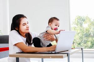 lycklig mamma med baby och arbetar med laptop, lycklig familj hemma mamma baby foto