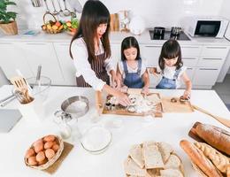 asiatisk mamma och söta två dotter förbereder degen för att göra en tårta i köksrummet hemma foto