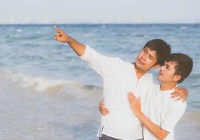 homosexuella porträtt ungt asiatiskt par stående pekar något tillsammans på stranden på sommaren, asien gay gå havet för fritid med romantiska och glada i semester till sjöss, hbt med juridiska koncept. foto