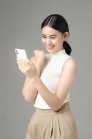 självsäker asiatisk kvinna som använder smartphone och tar emot goda nyheter från meddelandet på mobilchattapplikationen isolerad på grå bakgrund. porträtt av en vacker flicka i studion. foto