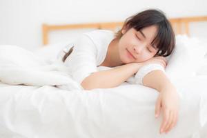vacker asiatisk ung kvinna trött sover liggande i sängen bekväm och glad, tjej med avkoppling och fritid i sovrummet, hälsa och välbefinnande koncept. foto