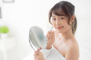 vackert porträtt ung asiatisk kvinna som tittar spegeln applicerar sminkläppstift på rummet, skönhetsläppar asiatisk flickmakeup och kosmetiskt mode på munnen hemma, livsstil och hälsokoncept. foto