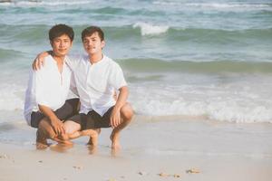 homosexuella porträtt ungt asiatiskt par sitter kram tillsammans på stranden på sommaren, asien gay turism för fritid och koppla av med romantisk och lycka i semester till sjöss, hbt juridiskt koncept. foto