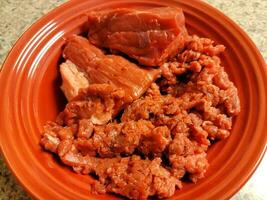 stora bitar och malet rått rött nötkött i röd skål foto
