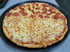 stor skivad pepperoni pizza med ost på bricka foto
