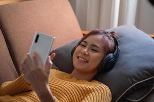 slappna av, stressa ner, semester, glad, asiatisk kvinna som kopplar av hemma och lyssnar på musik från smartphone och laptop glatt. foto