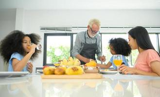 asiatisk-afrikansk amerikansk familj äter en god måltid tillsammans som inkluderar farfar, mamma och barn i husets matsal. foto