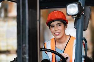 porträtt av en asiatisk kvinna med en gaffeltruck som används för att lyfta tunga föremål i ett lager. foto