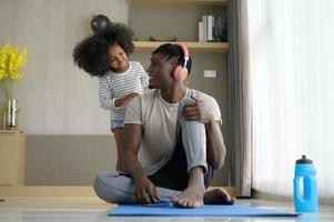 asiatisk-afroamerikansk far och son kopplar av och lyssnar på musik tillsammans efter yogaträning i vardagsrummet i huset. foto