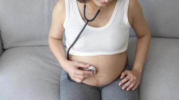 ung gravid kvinna att sätta stetoskop på mage, sjukvård och graviditetsvård koncept foto
