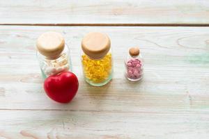 färgglada mediciner i glasflaskorna med rött hjärta på träbordet. diverse farmaceutisk medicin eller vitaminpiller, tabletter och kapslar foto