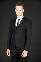 porträtt av ung smart och stilig affärsman i svart kostym som står på isolerad svart bakgrund. foto