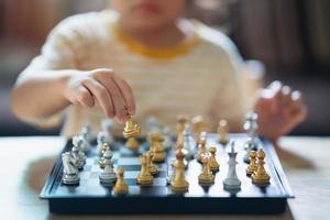 liten asiatisk baby som spelar schack i vardagsrummet hemma. smart kid. mode barn. litet genibarn. intelligent spel.schackbräde. baby aktivitet koncept. foto